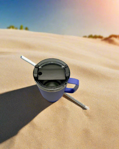 Blue insulated mug with straw on sand under a rainbow