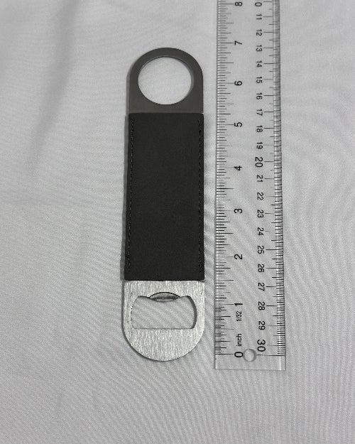 Bottle opener with leather strap on a gray surface with a ruler for scale.