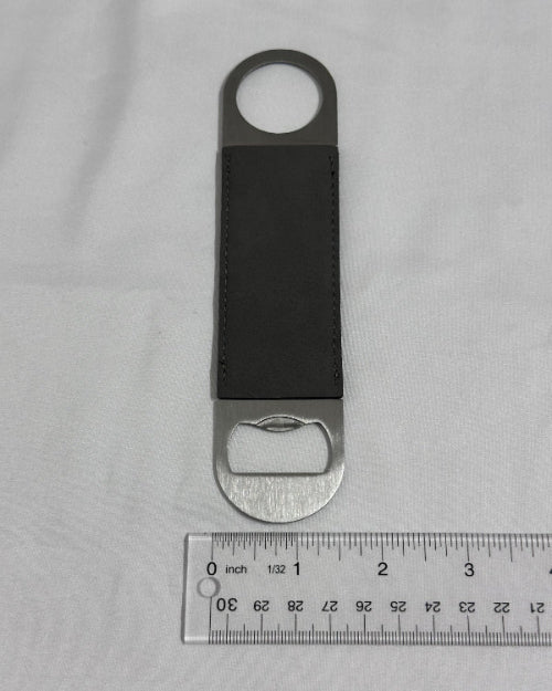 Leather bottle opener with silver cap on a gray background with a ruler for scale.