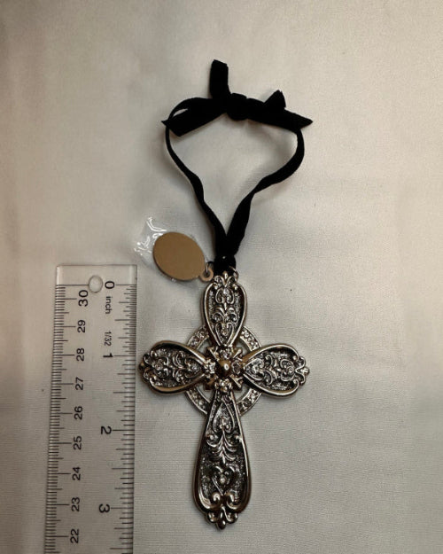 Decorative cross with black ribbon and tag on a white background with a ruler for scale.