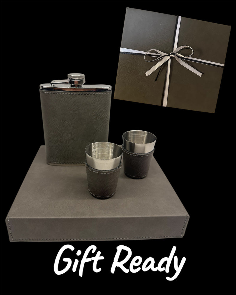 Gray flask and matching cups on a gray surface with a gift box in the background.