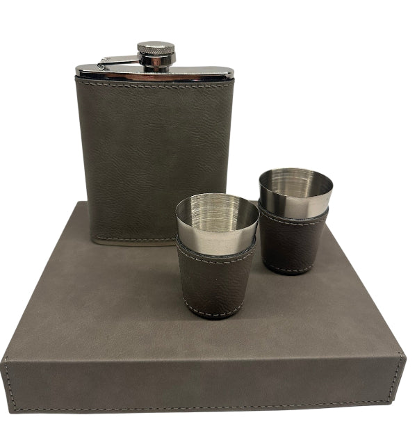 Brown leather flask and two matching shot glasses on a gray stand with a white background