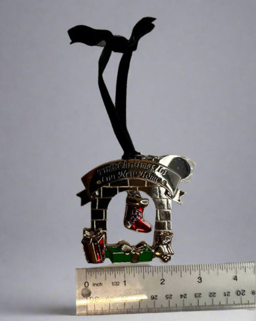 Silver charm with black ribbon and colorful accents on a white background with a ruler for scale.