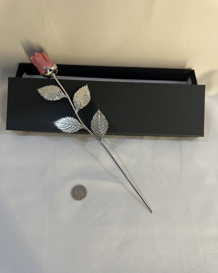 Silver rose with leaves on a white surface next to a black box.