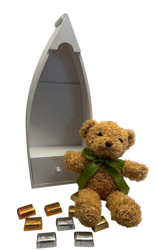 Teddy bear with a green ribbon sitting next to a small boat-shaped shelf on a white background
