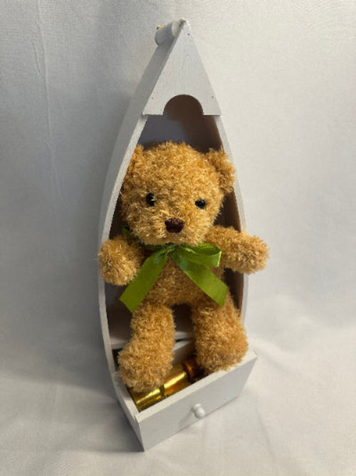 Brown teddy bear with a green bow in a white boat-shaped box on a light gray background