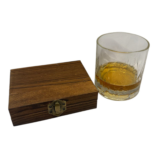 Wooden box with a brass clasp next to a glass of amber liquid on a white background