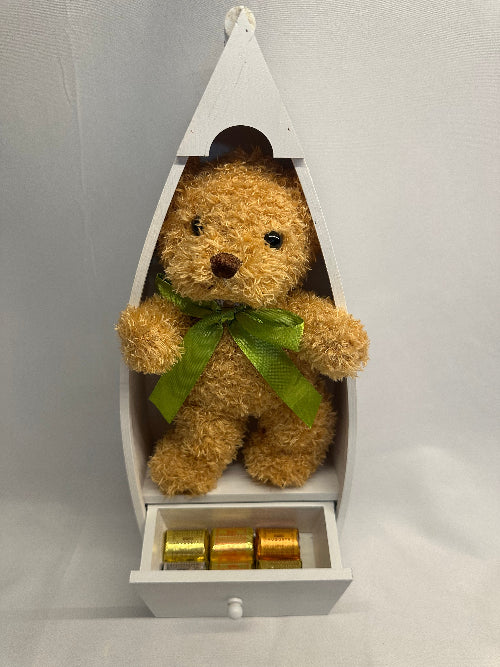 Brown teddy bear with a green ribbon inside a white decorative box on a light gray background