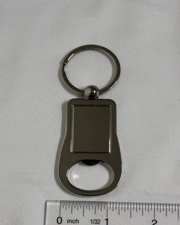 Keychain with bottle opener and key ring on a gray background with a ruler for scale.