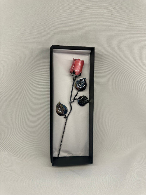 Pink rose with black leaves in a black box on a textured gray background
