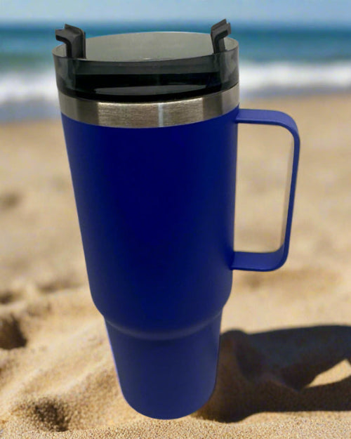 Blue travel mug with a black lid on a sandy beach