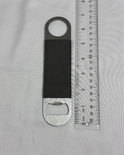 Bottle opener with leather strap on a gray surface with a ruler for scale.