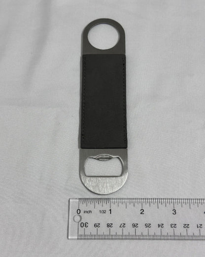 Leather bottle opener with silver cap on a gray background with a ruler for scale.