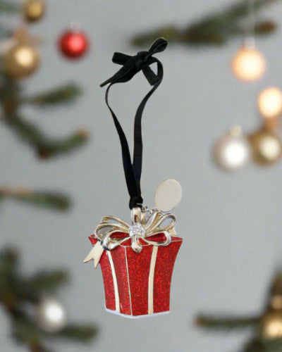 Red gift box ornament with a black ribbon against a blurred Christmas tree background