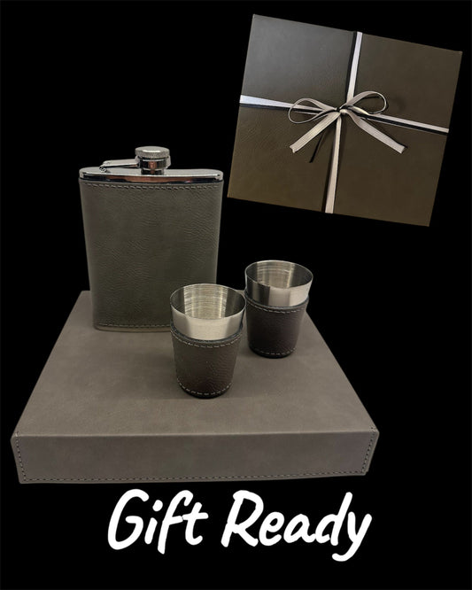 Gray flask and matching cups on a gray surface with a gift box in the background.