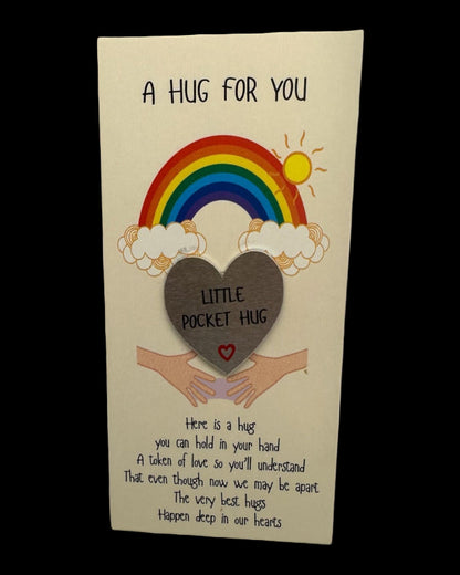 Card with a rainbow, heart, and hands holding a 'Little Pocket Hug' token on a beige background.