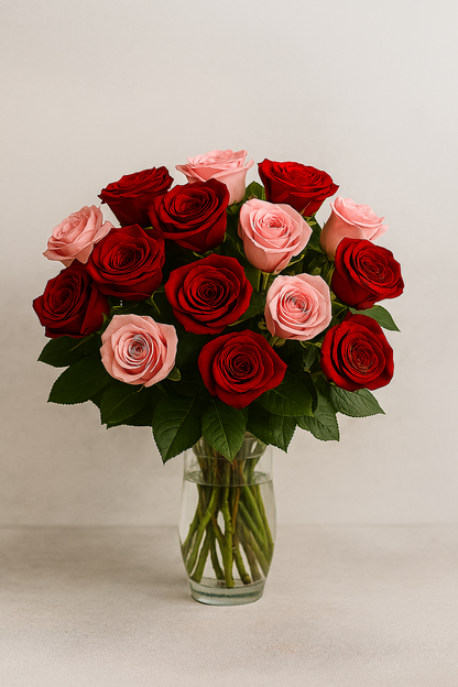 “Red and pink roses arranged in a clear glass vase, placed on a neutral beige surface with a soft off-white background. The bouquet includes fifteen fresh roses—eight red and seven pink—with lush green leaves, styled for emotional gifting and elegant presentation.”