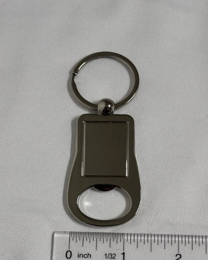 Keychain with bottle opener and key ring on a gray background with a ruler for scale.