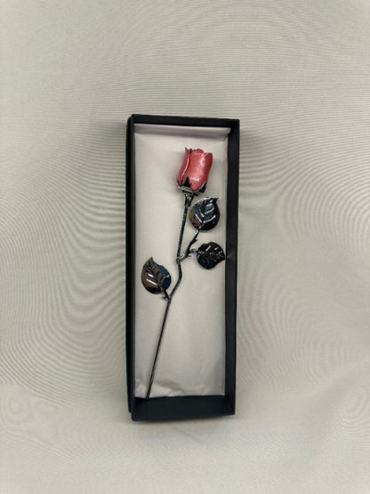 Pink rose with black leaves in a black box on a textured gray background